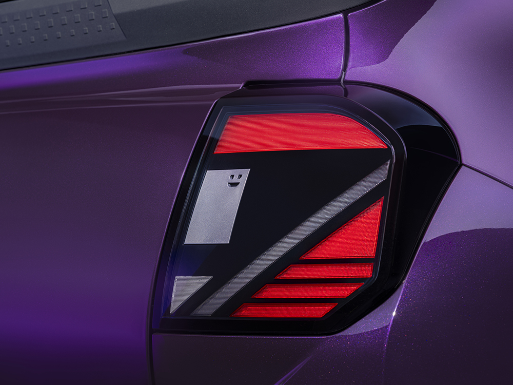 Photograph showing a close-up automotive taillight on a purple vehicle with bright red LED strips, a red upper band, silver geometric accents and robot face.